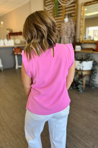 Woman wearing electric pink sleeveless top with light wash jeans, shown from behind in modern interior setting.