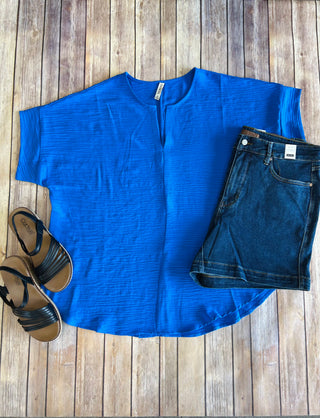 Bright blue v-neck blouse styled with denim shorts and black strappy sandals on wooden background