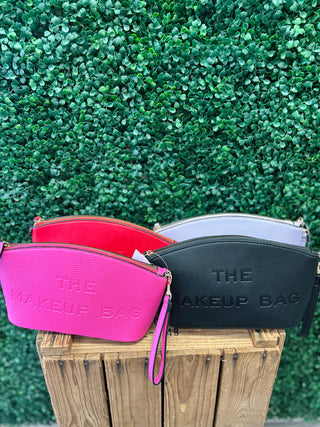 Embossed leather makeup pouches with zippers displayed on wooden surface against green foliage background.