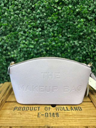 Pink embossed makeup bag with gold hardware sitting on wooden crate against green foliage background.