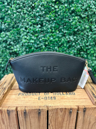 Black embossed makeup pouch with zipper displayed on wooden surface against green foliage background