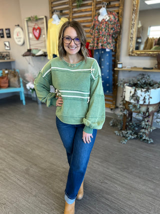 Woman wearing green striped pullover sweatshirt with jeans in boutique clothing store setting.