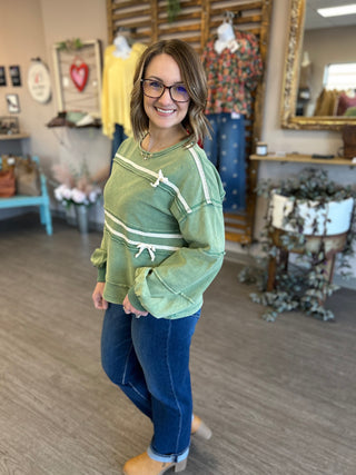 Woman wearing green pullover sweatshirt with white stripes and tie details in clothing boutique store.