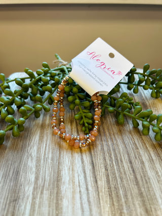 Era Bracelet by Alegria Accessories with amber and gold beads displayed on wood with green foliage