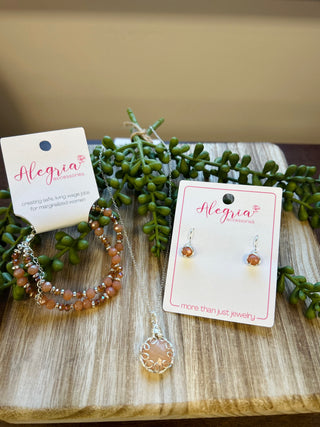 Alegria Accessories jewelry set with beaded bracelet, pendant necklace, and earrings displayed on wooden surface with gree...