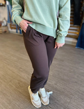 Person wearing soft brown joggers with mint green sweatshirt and white sneakers in casual pose