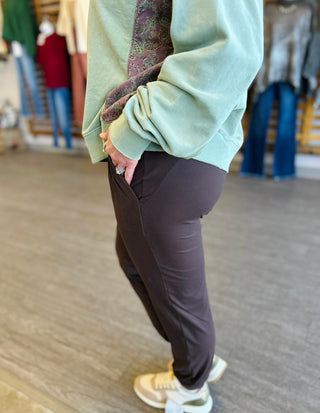 Woman wearing dark brown joggers with light green sweatshirt, standing casually with hand in pocket.