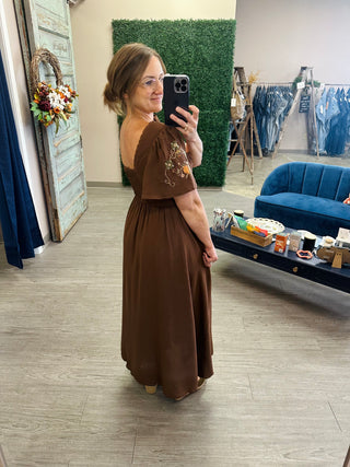 Woman wearing an embroidered bell sleeve midi dress with smocked back, posing in boutique mirror selfie.