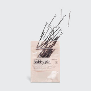 Black bobby pins spilling out of pink Kitsch Essential packaging against white background