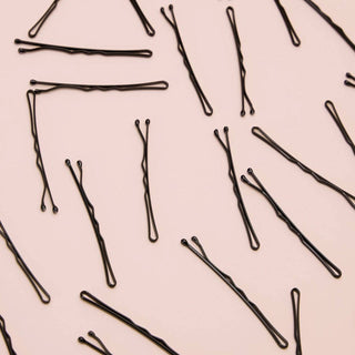 Black bobby pins scattered on pink background showing various lengths and styles from hair accessory set