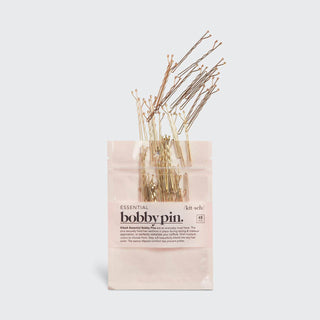 Package of blonde bobby pins with some pins spilling out of the pink cardboard packaging.