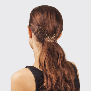 Woman with wavy brown hair styled in ponytail using gold bobby pins as decorative hair accessories.