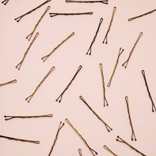 Scattered blonde bobby pins on pink background showing hair accessories for styling and securing hair.