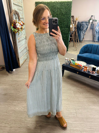 Woman wearing a sleeveless gingham midi dress with smocked bodice, paired with tan sandals.