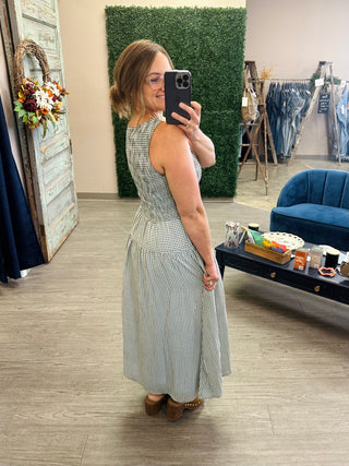 Woman wearing a sleeveless gingham midi dress with fitted bodice and full skirt, side view.