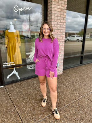 Woman wearing a matching ribbed long-sleeve top and drawstring shorts set with sneakers.