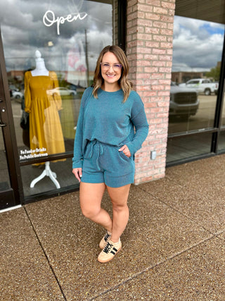 Woman wearing a matching ribbed long-sleeve top and shorts set with sneakers outdoors.