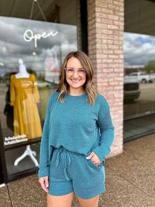 Woman wearing a matching ribbed long-sleeve top and shorts set, smiling outside a boutique.