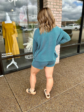 Woman wearing a matching ribbed long-sleeve top and shorts set with sneakers, back view.
