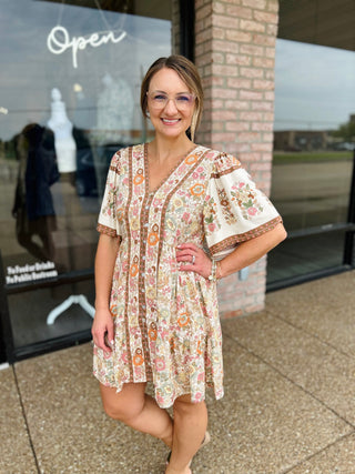 Woman wearing VERY J Fall Feels Floral Mini Dress with button front and flutter sleeves outdoors.