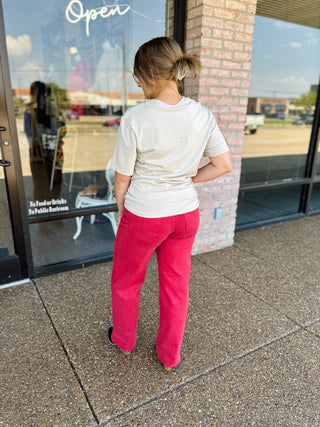 Woman wearing the Fall Vibes Tee with red jeans, shown from behind outside a boutique.