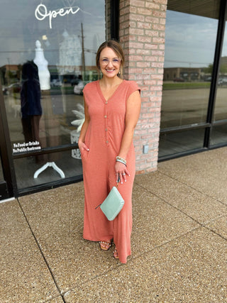 Woman wearing a striped sleeveless V-neck jumpsuit with button front, posing outside a boutique.