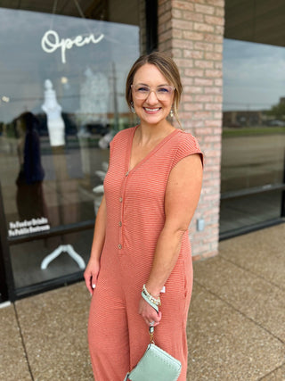 Woman smiling outside boutique wearing a striped button-front jumpsuit with cap sleeves.