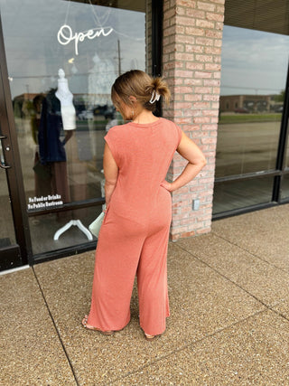Woman wearing a sleeveless wide-leg striped jumpsuit, posed outside a boutique storefront.
