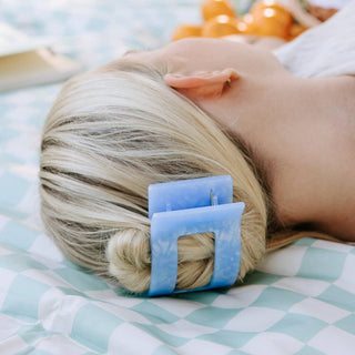 Woman lying down wearing a blue rectangular hair clip holding blonde hair in place