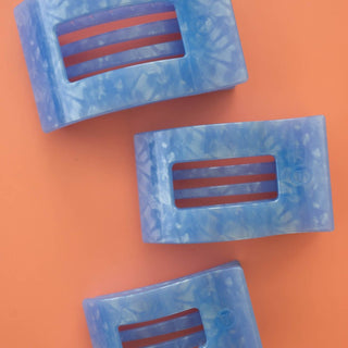 Three blue marbled rectangular hair clips with striped cutout centers on coral background
