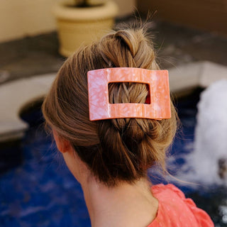 Woman wearing coral rectangular hair clip holding twisted bun hairstyle from behind