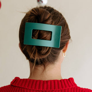 Woman wearing a large rectangular hair clip holding an updo hairstyle, shown from behind.