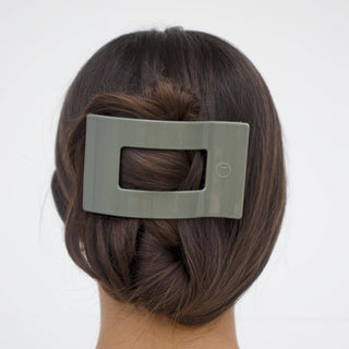 Woman wearing sage green rectangular hair clip with cutout center securing brown hair in low bun
