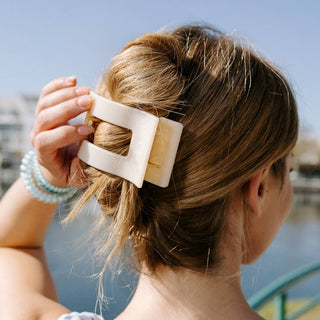 Woman wearing cream colored flat rectangle hair clip securing messy bun hairstyle outdoors