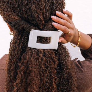 Woman with curly hair wearing a white rectangular hair clip with cutout detail