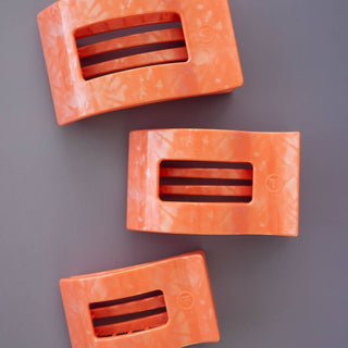 Three orange rectangular hair clips with ribbed grip design and cutout windows displayed on gray background.