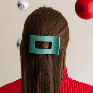 Woman wearing teal rectangular hair clip in brown hair with red sweater and holiday ornaments