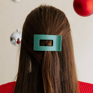 Person wearing a flat rectangular hair clip in brown hair with holiday ornaments in background