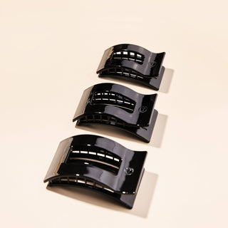 Three glossy black rectangular hair claw clips arranged diagonally in graduating sizes on neutral background.