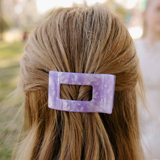 Woman wearing a purple marbled rectangular hair clip securing a half-up hairstyle with blonde hair.
