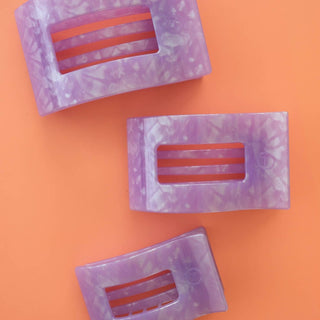 Three purple marbled rectangular hair clips with clear window cutouts displayed on orange background
