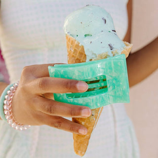 Hand holding mint green ice cream cone wearing translucent green rectangular hair clip with pearl bracelet