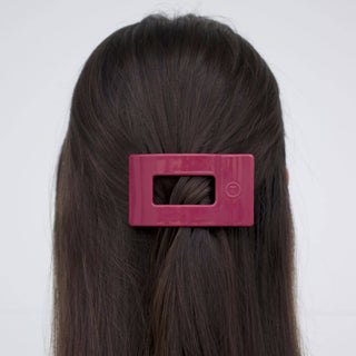 Person with long brown hair wearing a pink rectangular hair clip with cutout center