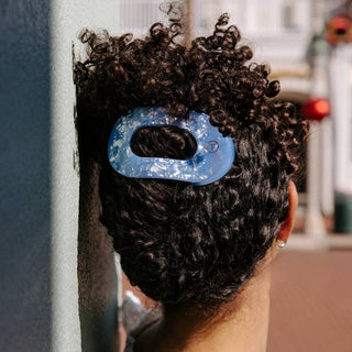 Person wearing a blue hair clip securing curly dark hair in a bun from behind.