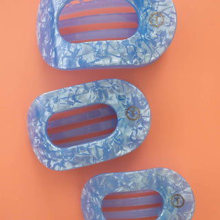 Three oval-shaped hair clips with crinkled blue finish and striped interior on coral background