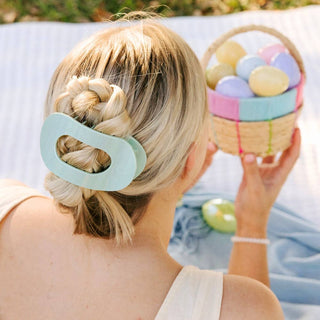 Woman wearing mint green flat round hair clip in twisted updo hairstyle while holding Easter basket