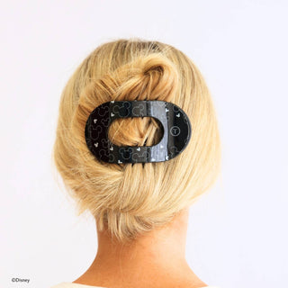 Woman wearing black Disney-themed flat round hair clip holding blonde hair in an updo bun style.