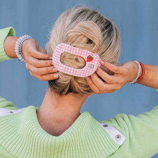 Woman styling hair in bun using pink gingham patterned flat round hair clip accessory