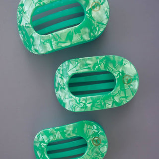 Three green marbled oval hair clips with horizontal slat openings arranged vertically on gray background.