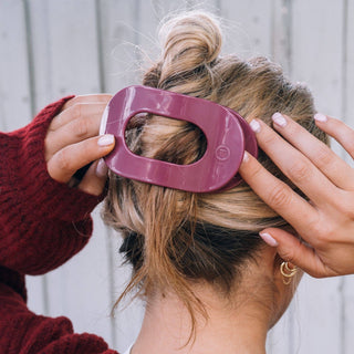 Woman securing messy bun hairstyle with purple flat round hair clip accessory